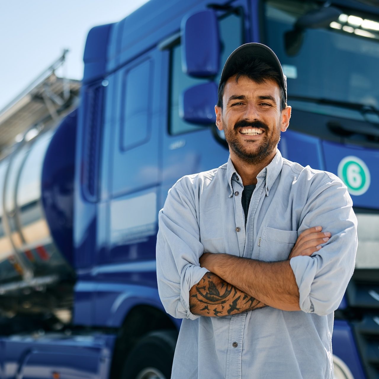 Confident truck driver in front of his vehicle looking at camera. Happy professional truck driver with arms crossed looking at camera.